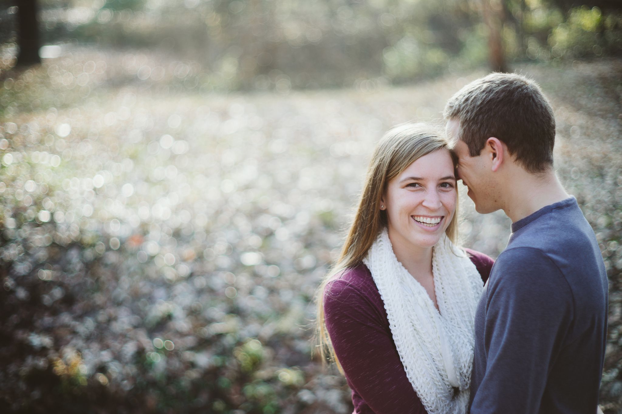 A man in a blue long sleeved shirt whispers into a woman's ear. She is giggling at what he is saying. 