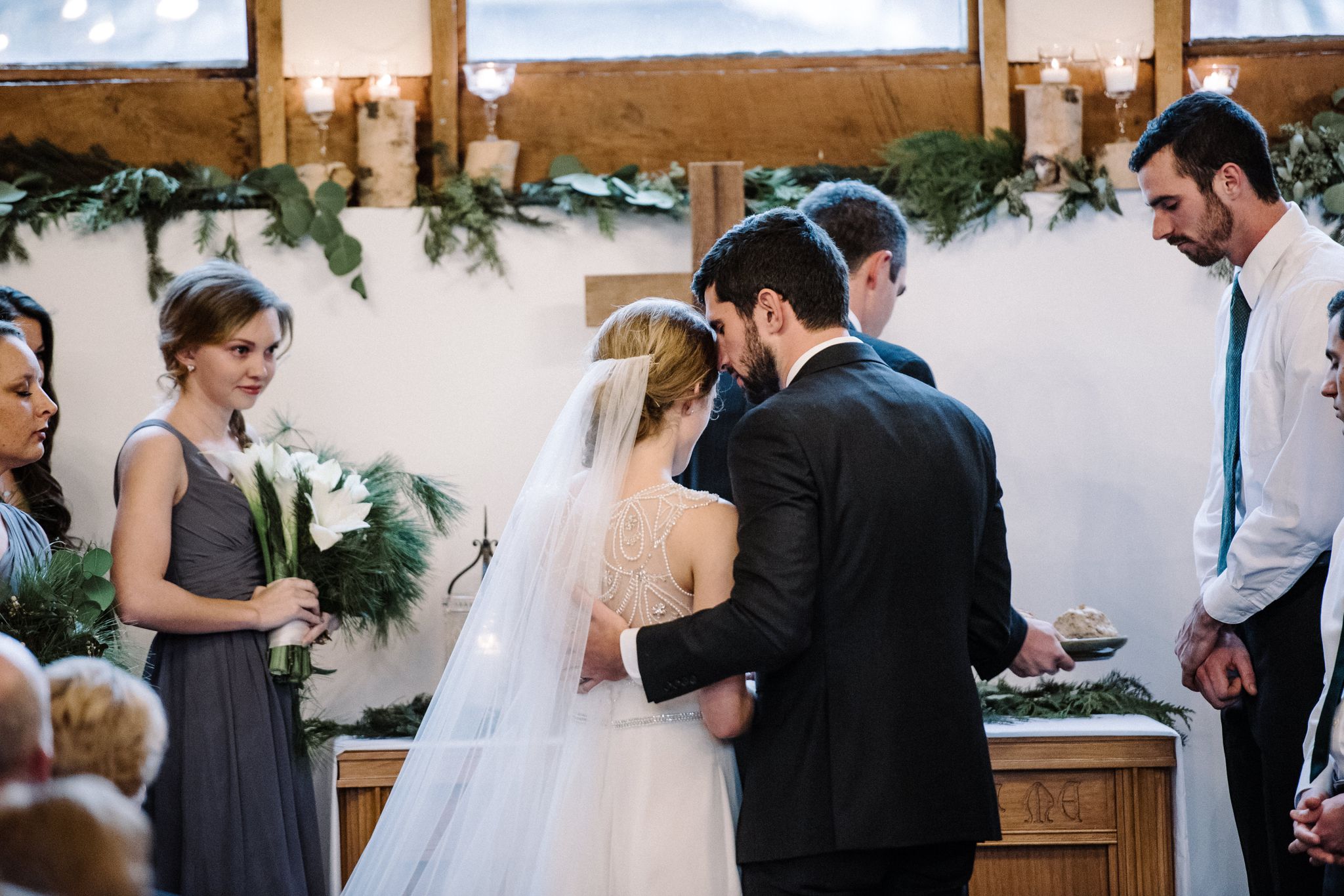 A groom whispers into the bride's ear while the maid of honor watches.