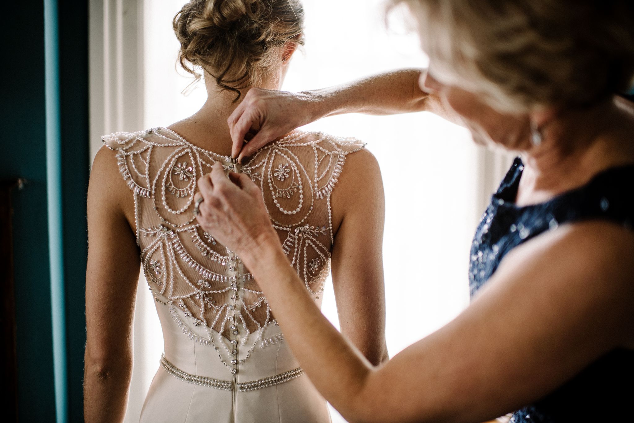 A bride's mom fastens the buttons on the back of her wedding gown.
