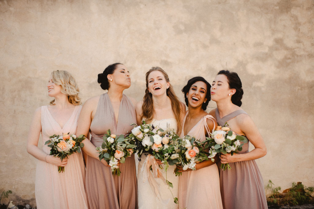 candid photo of bridesmaids laughing and air kissing each other