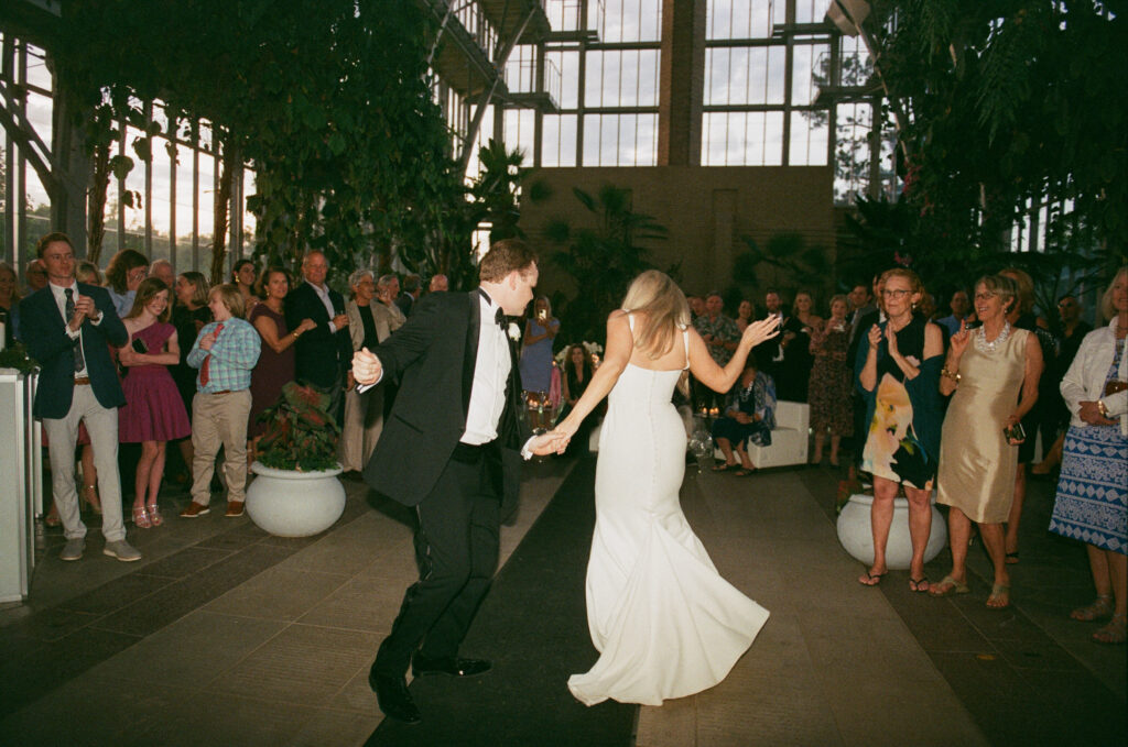 Documentary wedding photo of a bride and groom dancing to disco for their first dance as guests circle around them on the dance floor and clap along.