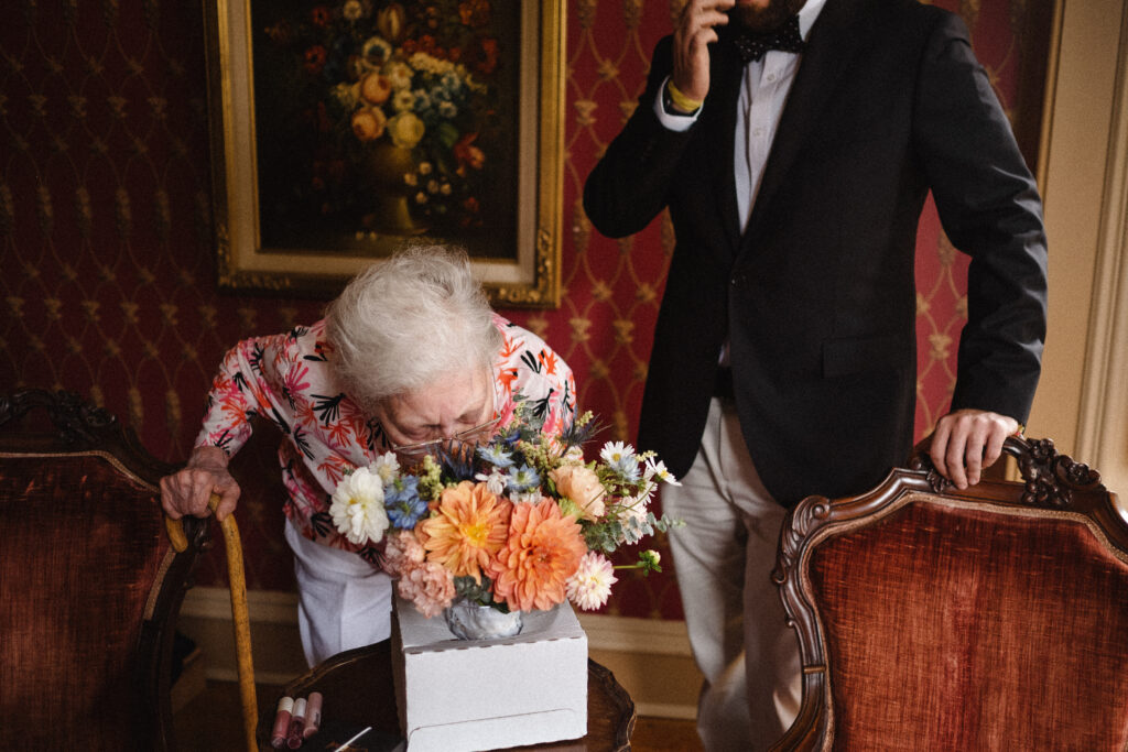 candid photo of a bride's grandmother bending down to smell her bouquet of flowers