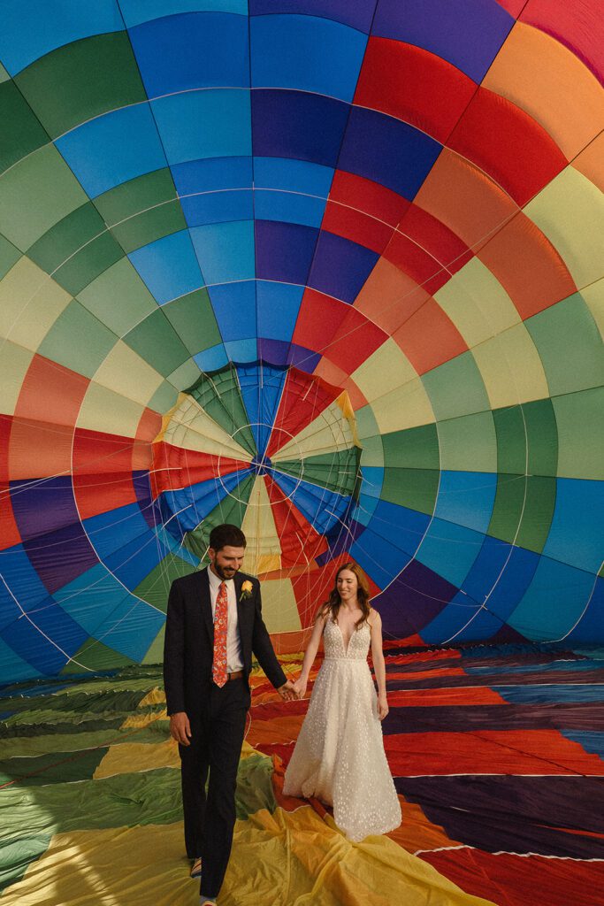 A man and woman holding hands in front of a hot air balloon.
